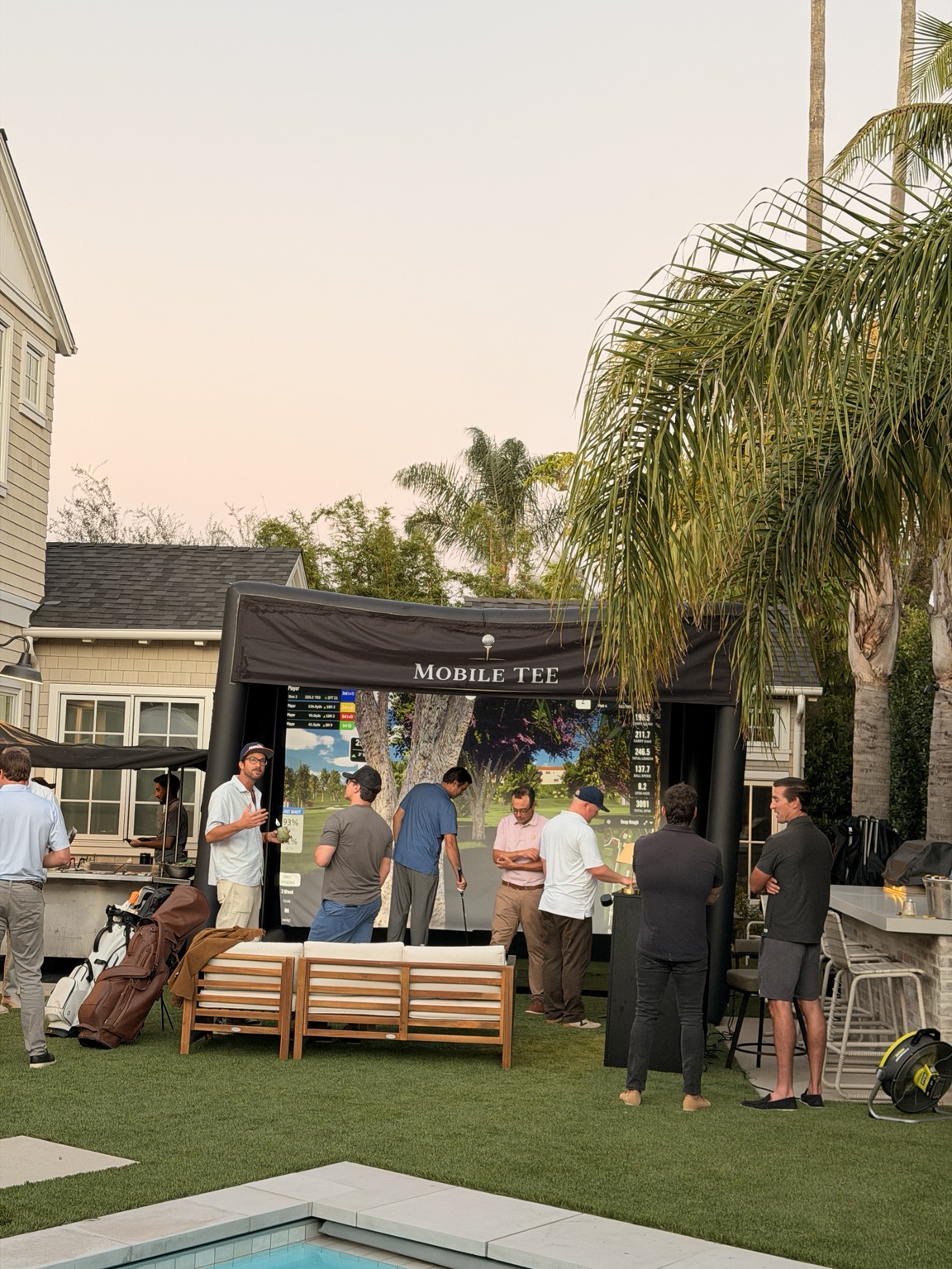 Guests gathered around the Mobile Tee golf simulator at a backyard celebration